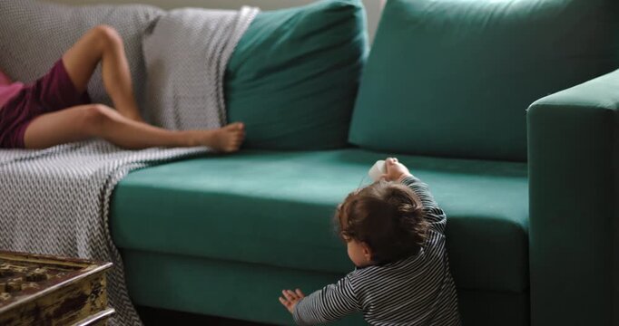 Toddler learns to stand by holding the sofa at home, briefly losing balance before recovering independently in a childhood milestone of mobility, confidence and resilience