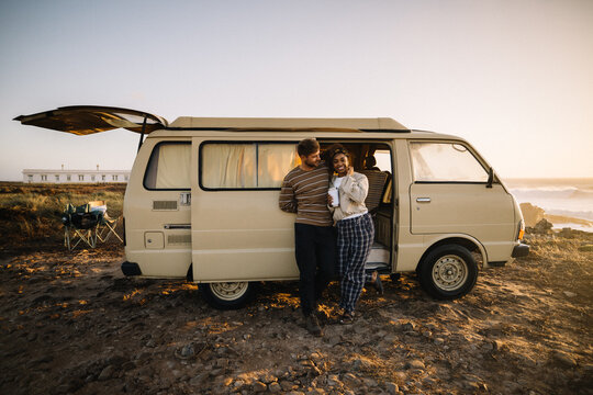 A couple shares a moment near a vintage van on a sunset beach trip