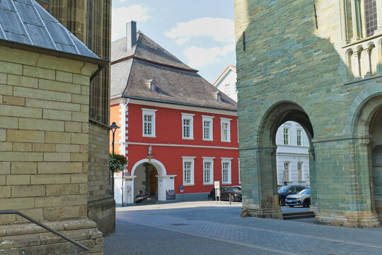 An architectural street scene in Soest, Germany. A vibrant red building with a white trimmed archway stands between two ancient stone structures - Soest, Westphalia, Germany