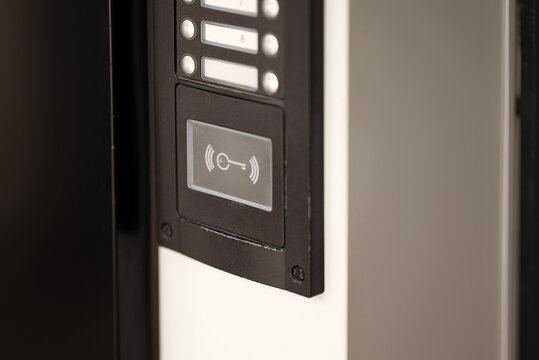 Modern black intercom access control panel with RFID contactless key reader and call buttons. Security system at residential building entrance door.