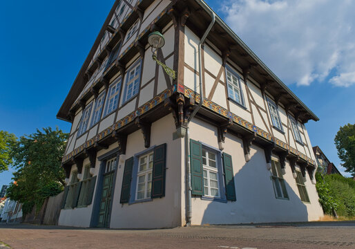 A charming traditional half-timbered house with white walls, dark beams, and green shutters, seen from a low angle against a bright blue sky - Soest, Westphalia, Germany