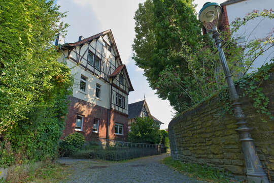 A charming street scene in an old European town features a half-timbered house beside an uphill path with a vintage streetlamp and stone wall - Soest, Westphalia, Germany