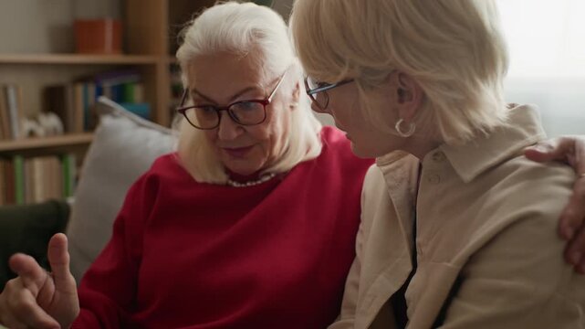 Caucasian senior woman and middle aged daughter sitting together, using smartphone. Video is perfect for senior care services, digital literacy campaigns, or family communication apps