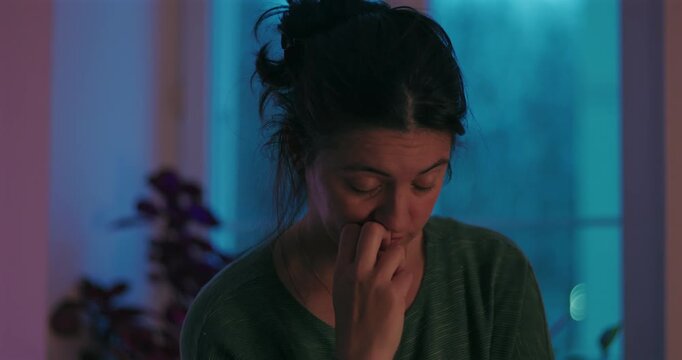 Concerned woman touches her face and gazes around while deep in thought by a window at home, expressing worry, indecision and emotional strain during personal reflection