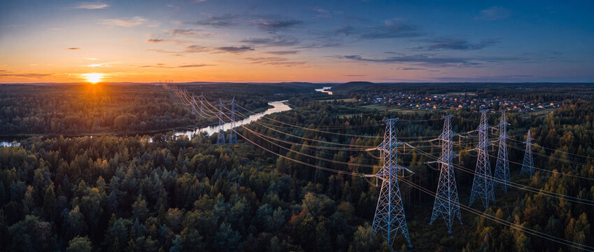 Power lines over forest at sunset features steel transmission towers stretching across a dense pine landscape near a river, perfect for energy grid and utility development concepts