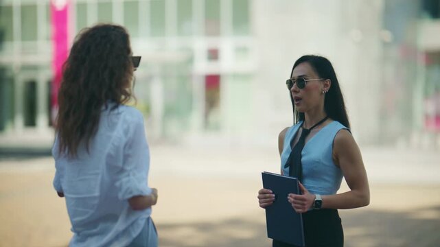 Two businesswomen engage in an outdoor meeting, discussing important matters with a professional demeanor. They shake hands to finalize their agreement in an urban setting.