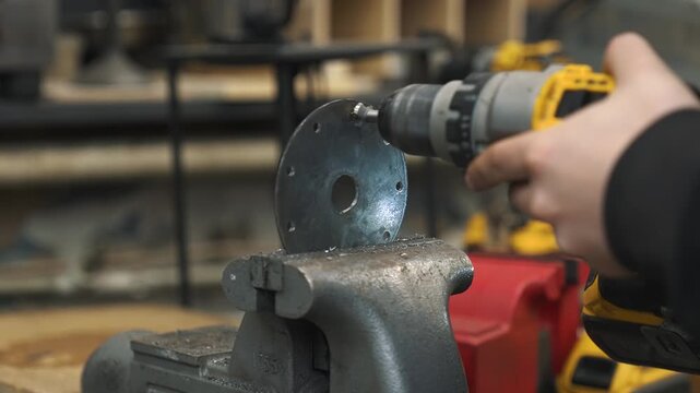 An engineer drills holes in a steel plate that will serve as the core for a gear train with a sprocket and chain.