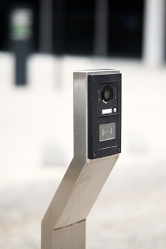 Modern outdoor intercom panel with security camera and contactless key reader mounted on steel post. Access control device for gated property entrance.