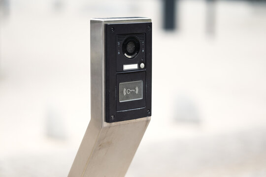 Modern outdoor intercom panel with security camera and contactless key reader mounted on steel post. Access control device for gated property entrance.