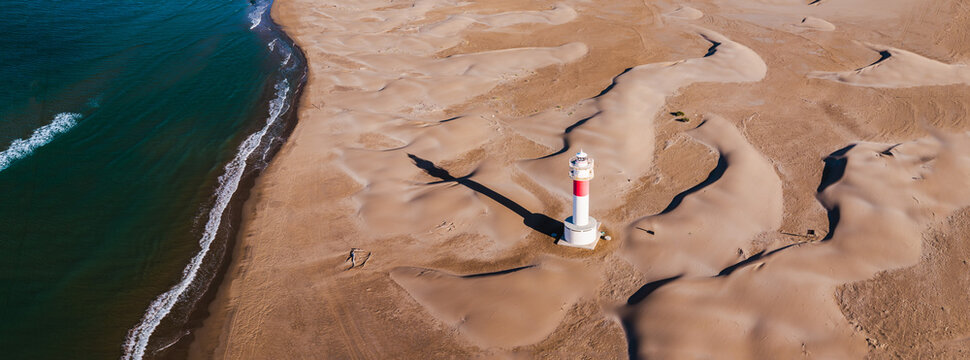 Aerial view of Fangar Lighthouse casting a long shadow across sand dunes on the Mediterranean coast in the Ebro Delta