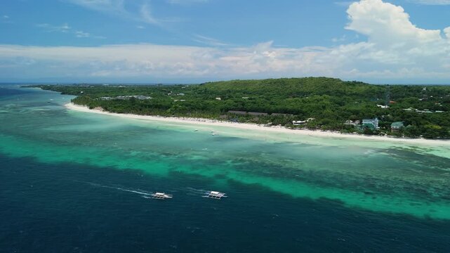 Aerial drone follows two longboats driving over deep blue water along Dumaluan Beach, revealing reef flats, white sand, and the Panglao coastline in Bohol
