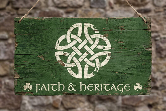 Rustic distressed green wooden sign hanging by a rope against a blurred stone wall background. Features a chipped white painted Celtic knot, shamrock, and Faith & Heritage text in vintage typography.