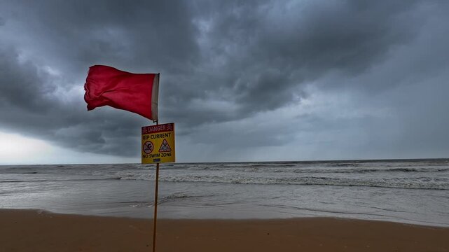 Red warning flag and danger sign on a stormy beach with rough sea and dark clouds