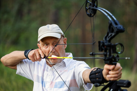 Senior man practicing archery with compound bow in forest