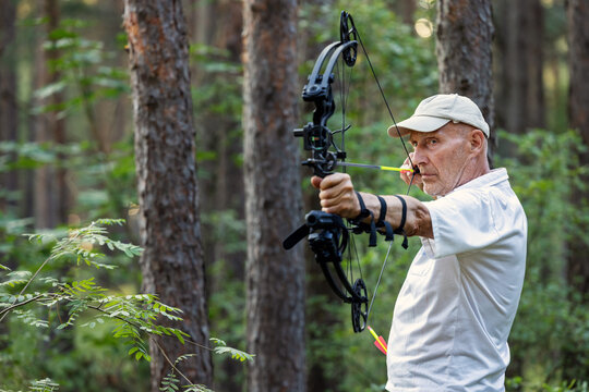 Senior man practicing archery with compound bow in forest