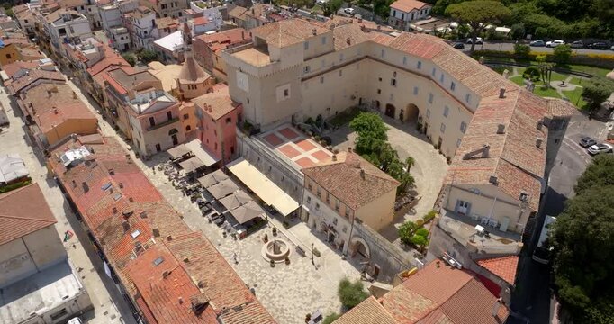 High aerial view of the historic main square and Templar tower in San Felice Circeo, Italy, surrounded by traditional terracotta roofed buildings and lively outdoor cafes on a sunny day.
