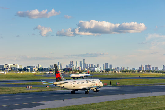 Two Air Canada passenger aircraft taxi at Toronto Pearson airport before the skyline.