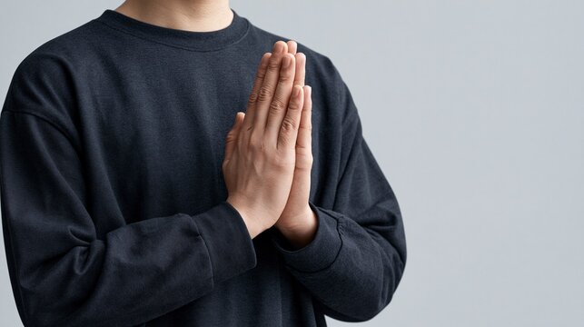 Person with hands clasped in prayer gesture against a plain background
