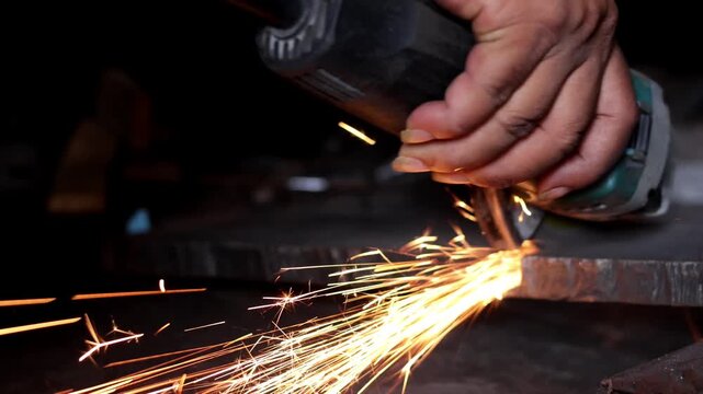 A worker using a power tool to grind and cut steel with flying hot sparks in a workshop.