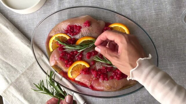 preparing chicken fillet for baking with rosemary sprigs red currants and orange slices creating fresh culinary composition concept of healthy cooking food styling recipes and gastronomy