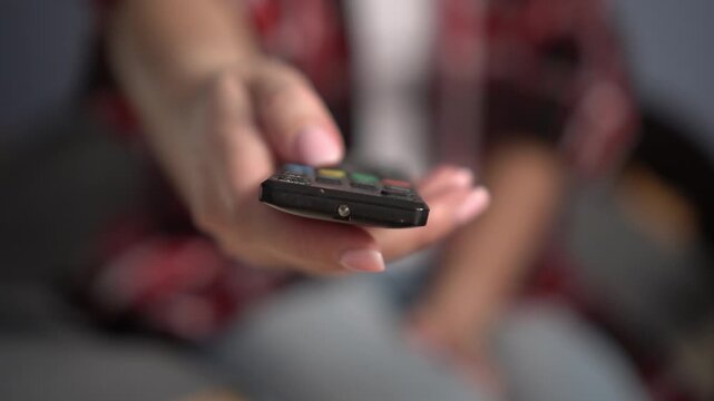 Close-up of female hands holding a TV remote control. Hand pressing remote control. Watching TV