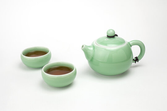 Traditional light green celadon ceramic teapot with two teacups filled with hot tea isolated on white background