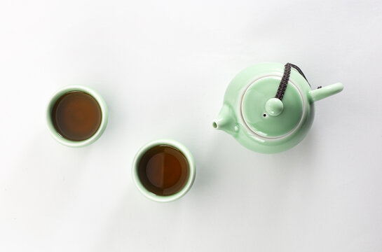 Traditional light green celadon ceramic teapot with two teacups filled with hot tea isolated on white background