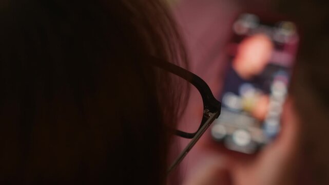 Close-up of a woman browsing social media on a smartphone with focus on her head while the mobile phone remains blurred in the foreground. Concept of digital lifestyle, mobile communication, online en