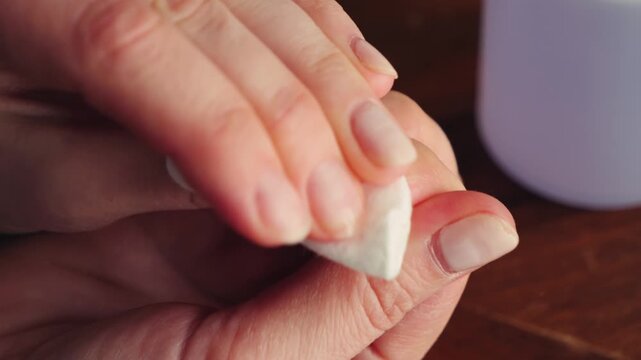 Close-up of a woman removing nail polish from her fingernails with a cotton pad and nail polish remover. Manicure removal, nail care and beauty routine at home. High quality 4k footage
