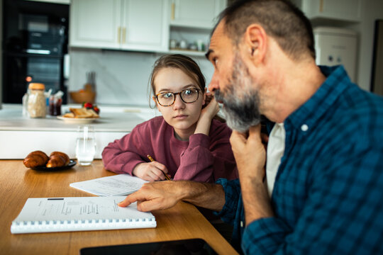 Father helping teenage daughter with math homework at kitchen table