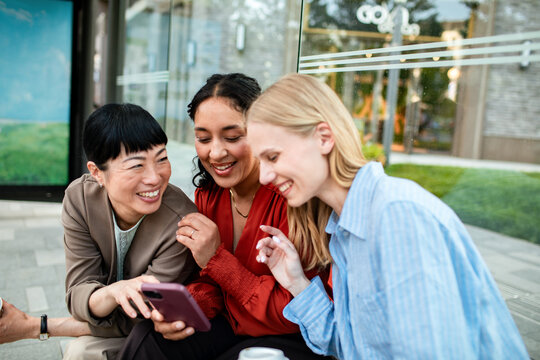 Three women friends looking at smartphone outdoors