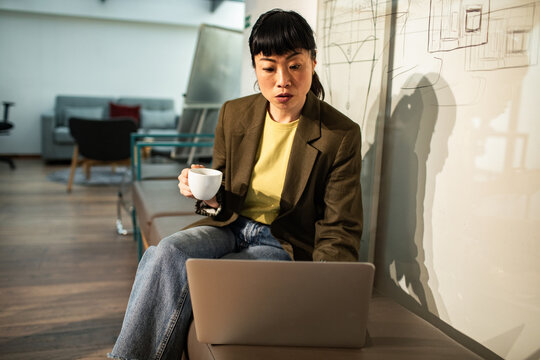 Woman working on laptop with coffee in modern office lounge