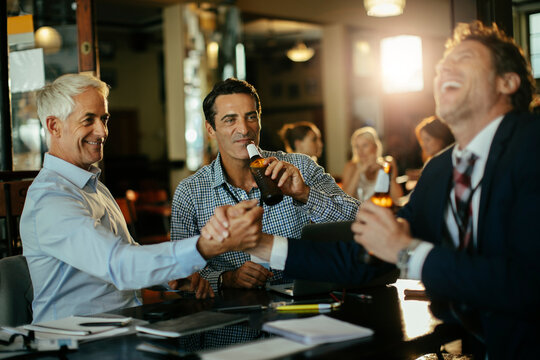 Three business colleagues celebrating deal with beers at bar