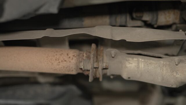 A rusty spring-loaded flange joint connecting parts of a car exhaust pipe.