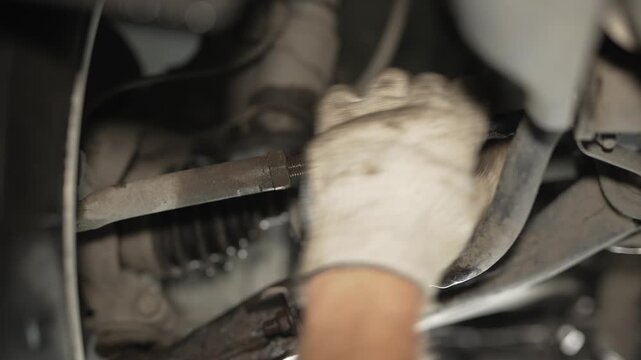 A mechanic in a white work glove adjusts a car steering tie rod during alignment.