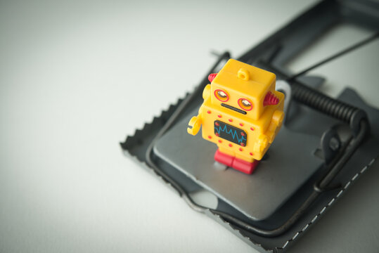 Close up AI robot toy in a rat trap on grey background. Artificial intelligence (AI) bubble, rapid speculation in stock market but low revenue, loss investment, investment trap in tech company concept