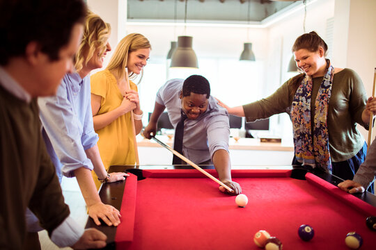 Coworkers playing billiards together in modern office