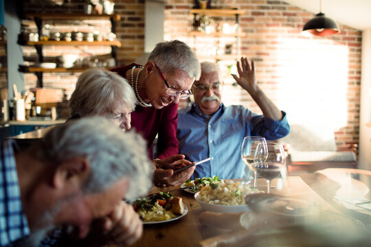 Senior friends laughing over smartphone during home dinner