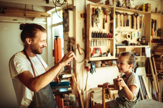 Smiling woodworker teaching child in carpentry workshop