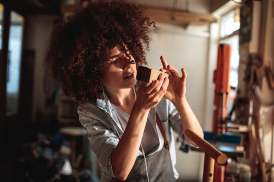 Focused craftswoman inspecting wood block in workshop