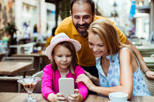 Smiling family looking at smartphone at outdoor cafe