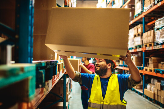 Warehouse worker lifting box on rack in distribution center