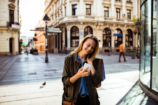 Smiling young woman using smartphone on european city street