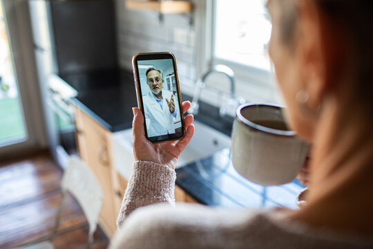 Woman video calling doctor in home kitchen