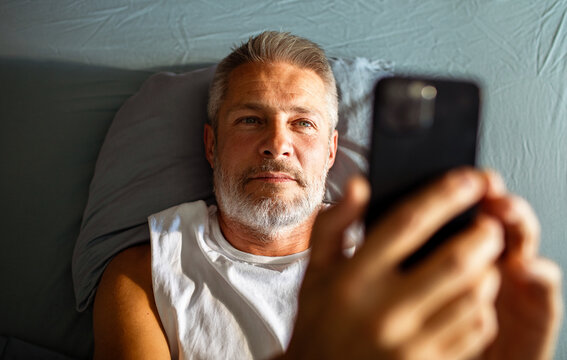 Mature man lying in bed using smartphone at home