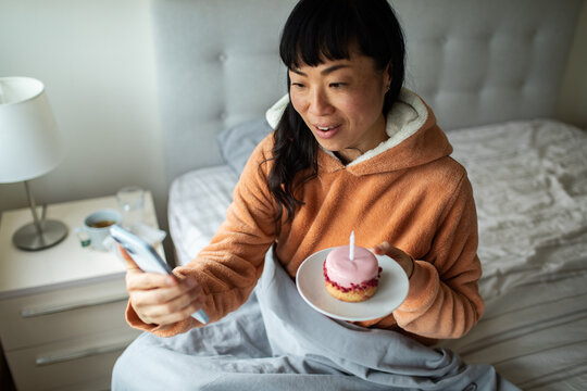 Woman video calling with birthday cupcake in bed at home
