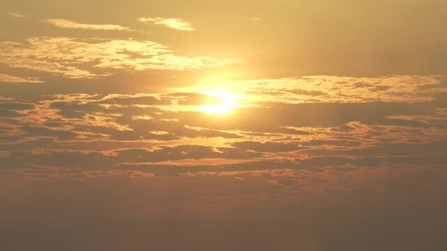 Bright morning sun shining through layered clouds in a warm golden sky.