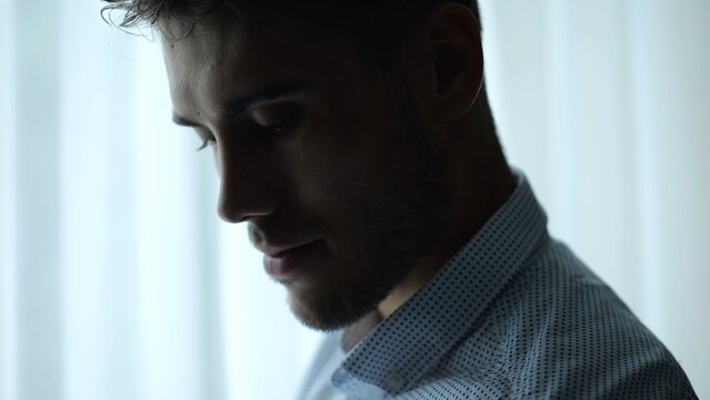 Close up portrait of young entrepreneur standing near large window in modern office and working on notebook. Handsome businessman in shirt using notebook for job with bright day light at background