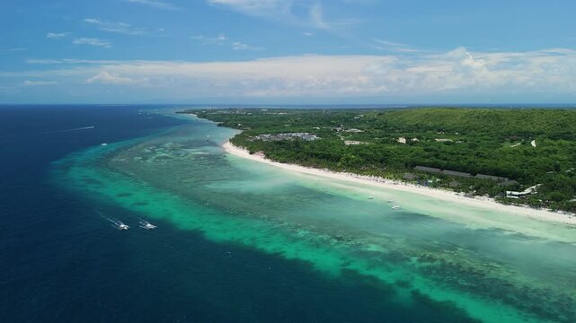 Aerial ascends and pulls back from two longboats driving along Dumaluan Beach, revealing reef flats, white sand, turquoise water, and the Panglao coastline in Bohol