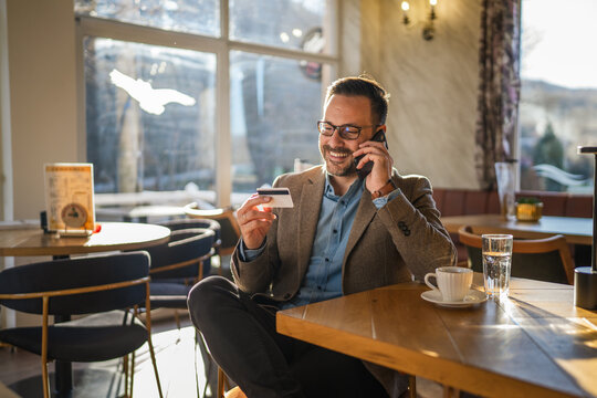 Man talking on phone and holding credit card in cafe